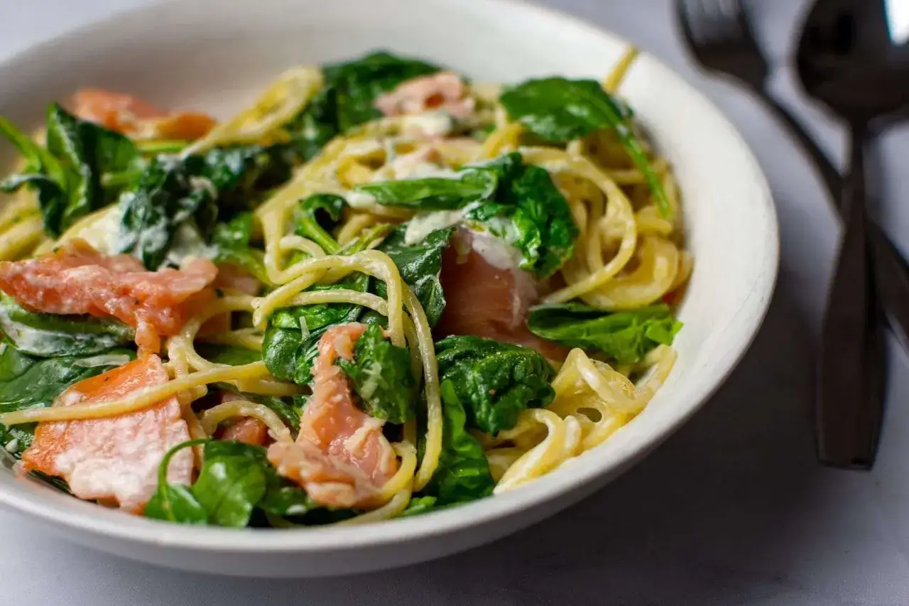 Eine Schüssel mit cremigen Nudeln mit Lachs und frischem Spinat.