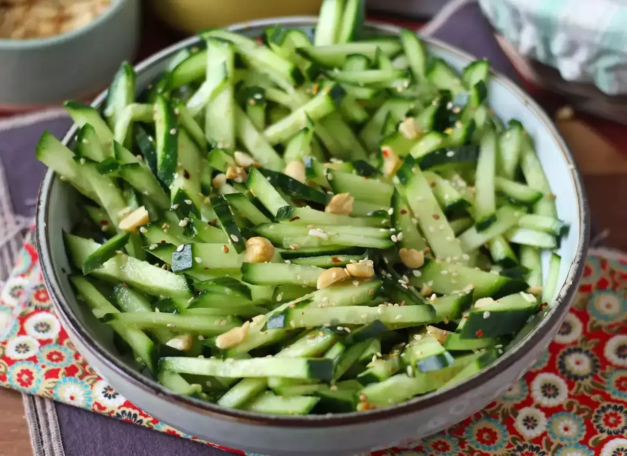 Una ciotola piena di fresca insalata di cetrioli tagliati a julienne, condita con semi di sesamo e arachidi croccanti.