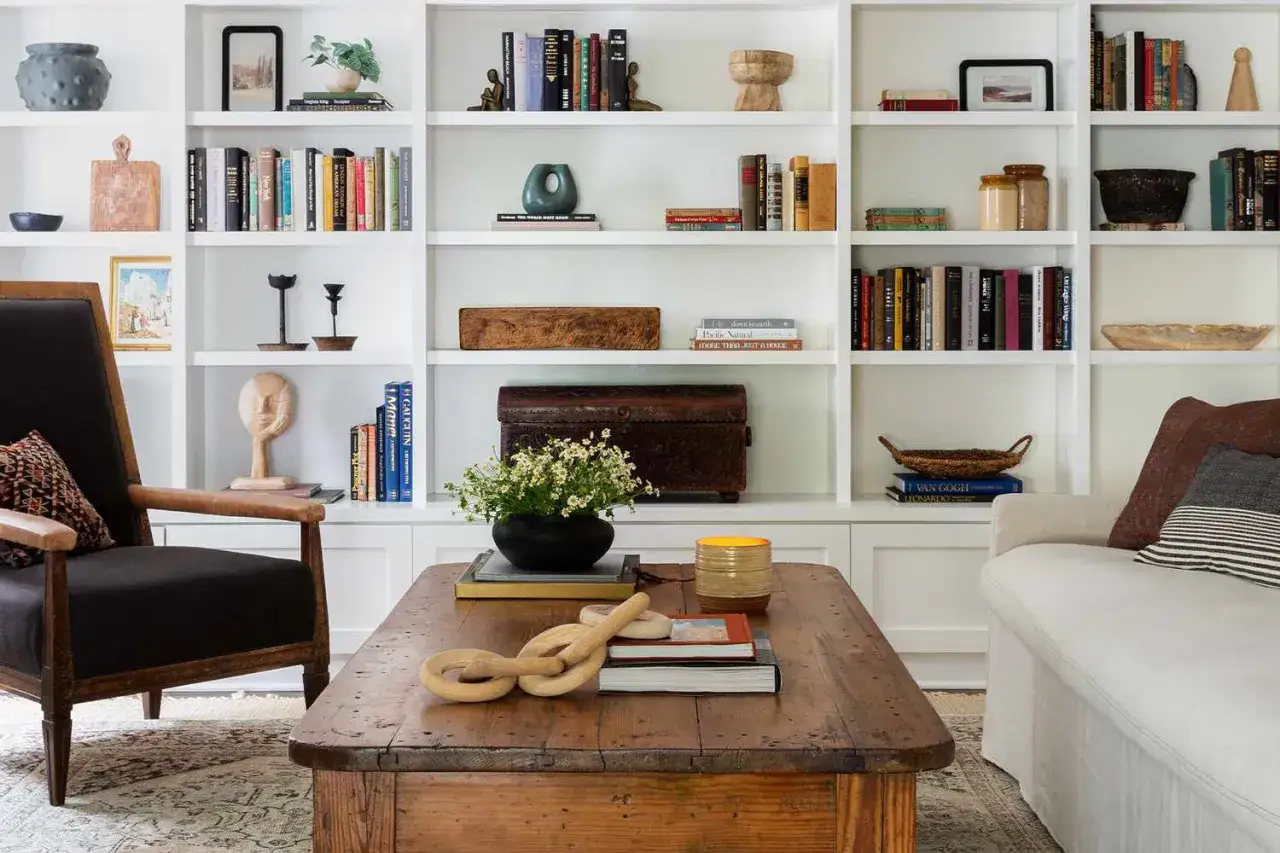 Une bibliothèque salon avec des livres, des objets décoratifs et un fauteuil confortable. Une idée pour une bibliothèque salon chaleureuse et stylée.