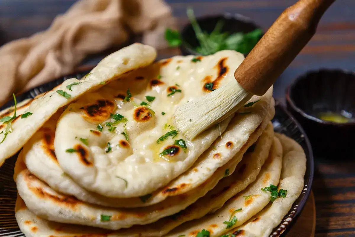 Frisch gebackenes naan brot wird mit Butter bestrichen und mit Koriander bestreut.