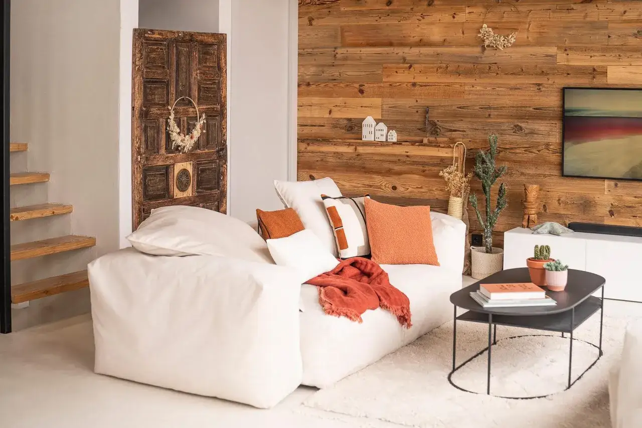 Un salon cosy avec un grand canapé blanc, des coussins orange et un plaid. Une porte ancienne décore le mur.
