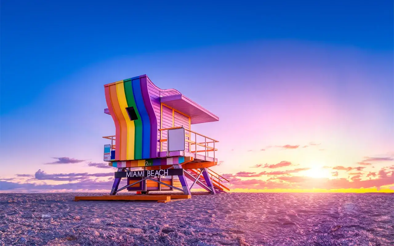 A rainbow-painted lifeguard tower stands on Miami Beach at sunset, a vibrant symbol of inclusivity.