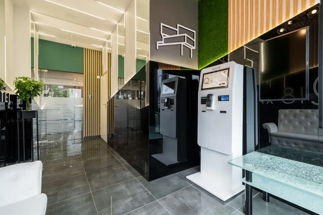 Nowoczesny hotel z terminalem do wcześniejszego zameldowania w hotelu. W holu znajduje się biały automat samoobsługowy, zielona ściana z mchu i elegancka sofa.