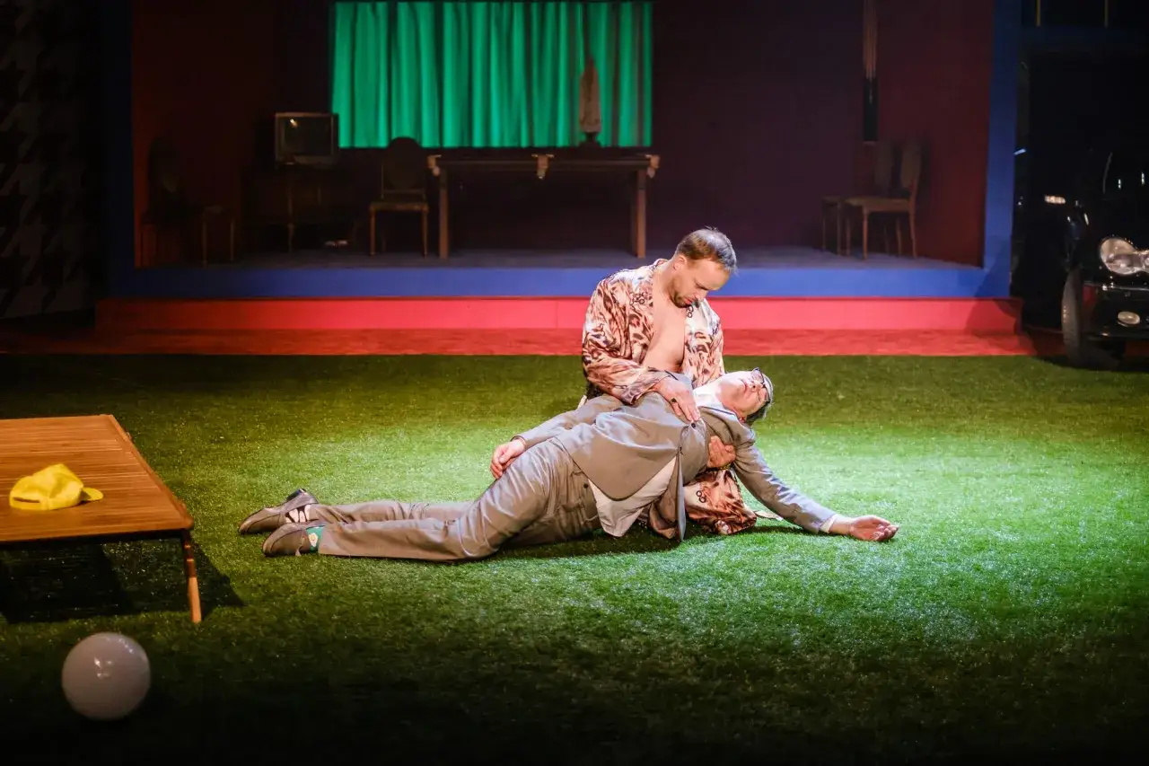 Scena teatralna z dwoma mężczyznami, jeden leży na drugim. Może to być nawiązanie do dorobku literackiego Moliera, ukazujące jego ponadczasowe tematy.