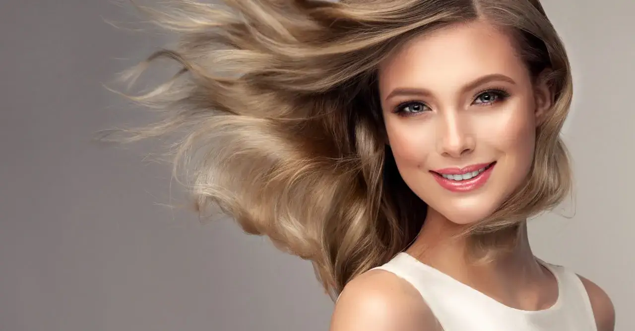 Lächelnde Frau mit voluminösen, mittelblonden Haaren, die im Wind wehen.
