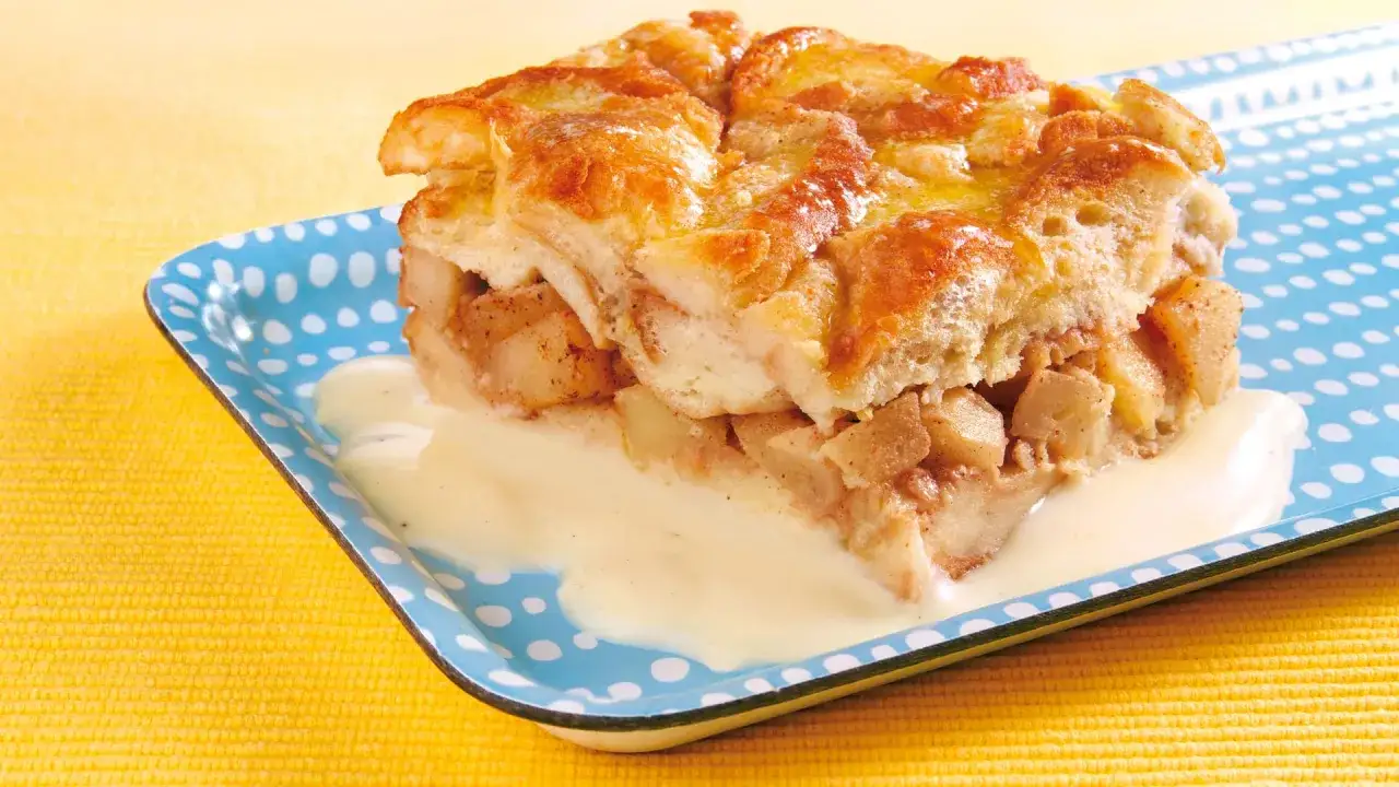 Ein St&uuml;ck Apfel-Scheiterhaufen mit Vanillesauce auf einem blauen Teller mit Punkten. Ein k&ouml;stliches Rezept f&uuml;r den perfekten Scheiterhaufen.