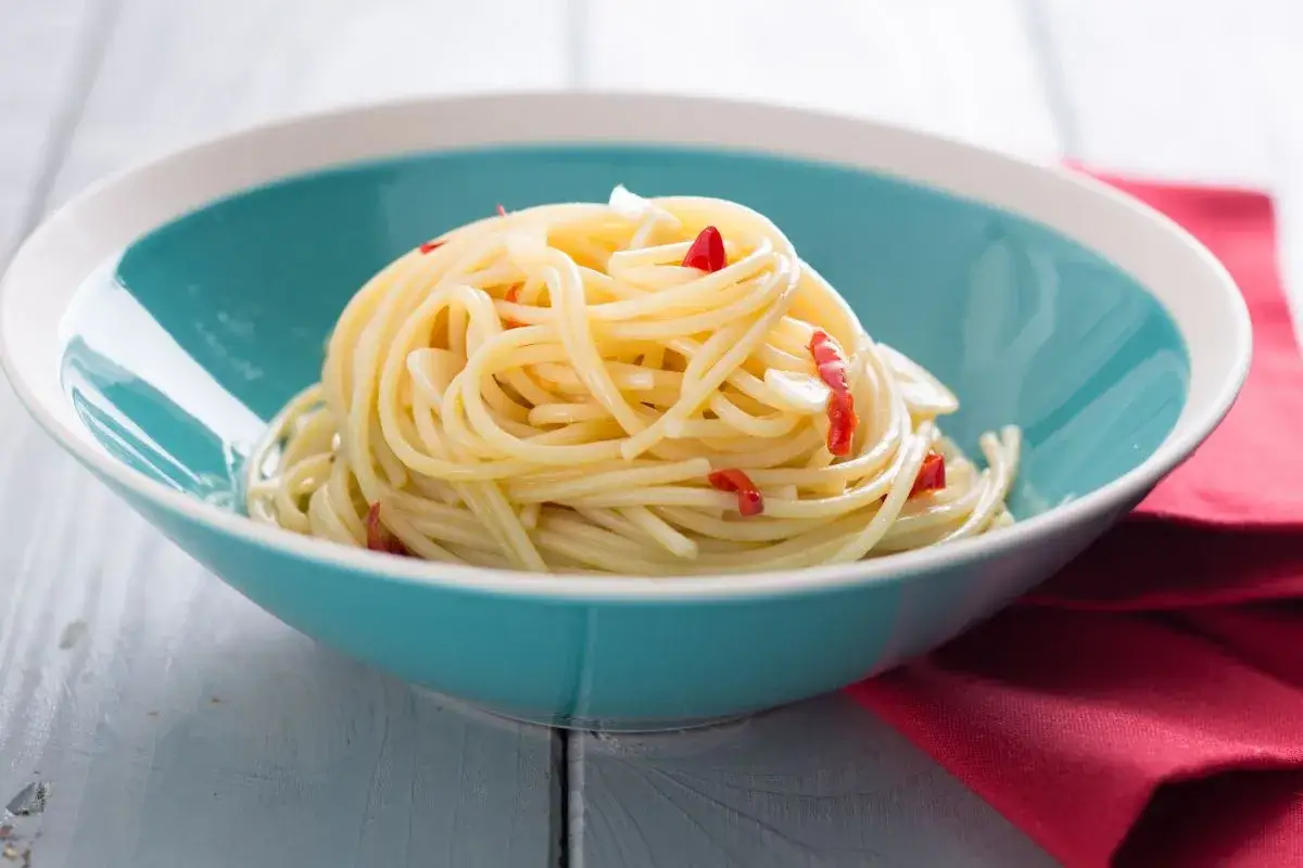 Porcja spaghetti aglio e olio peperoncino w turkusowej misce, z widocznymi kawałkami czosnku i papryczki chili.