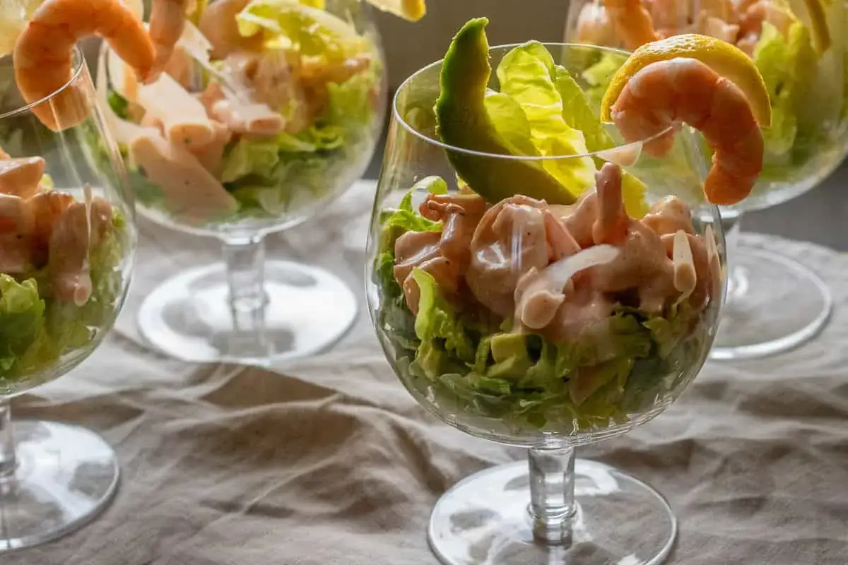 Erfrischender Krabbencocktail mit Avocado und knackigem Salat in eleganten Gl&auml;sern, garniert mit Garnelen und Zitronenspalten.