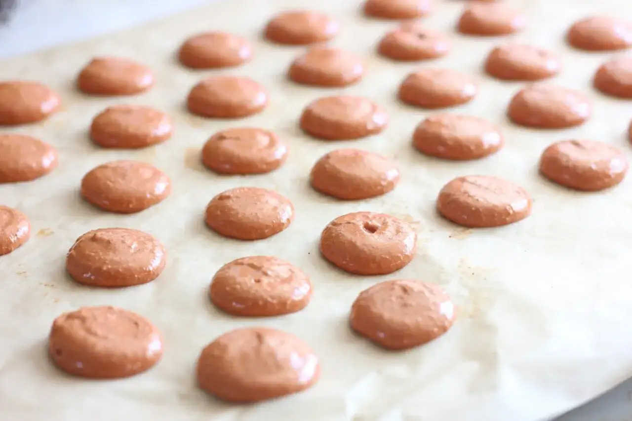 Petits macarons bruns prêts pour la cuisson. La chaleur tournante assurera une cuisson uniforme pour des coques parfaites.