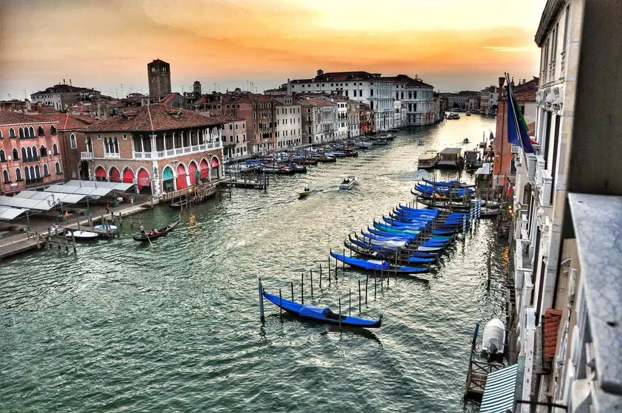 Widok na Canal Grande w Wenecji o zachodzie słońca. Widać liczne gondole, łodzie i zabytkowe budynki. Idealne miejsce, by zobaczyć, co zobaczyć w Wenecji.