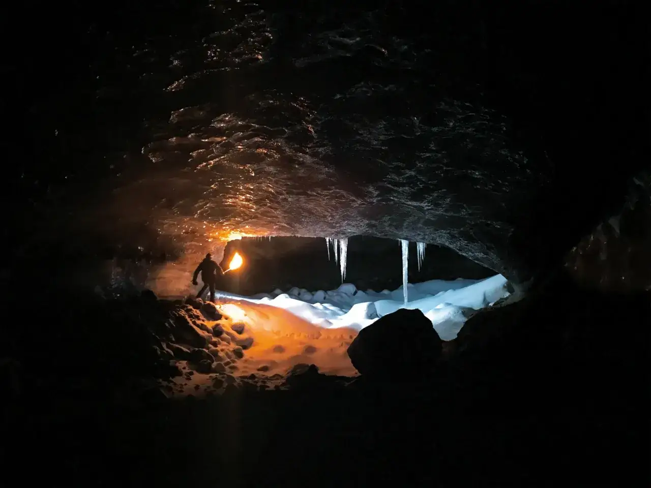 Oświetlona pochodnią jaskinia lodowa, uchwycona w trybie nocnym iPhone. Widać stalaktyty i śnieg.