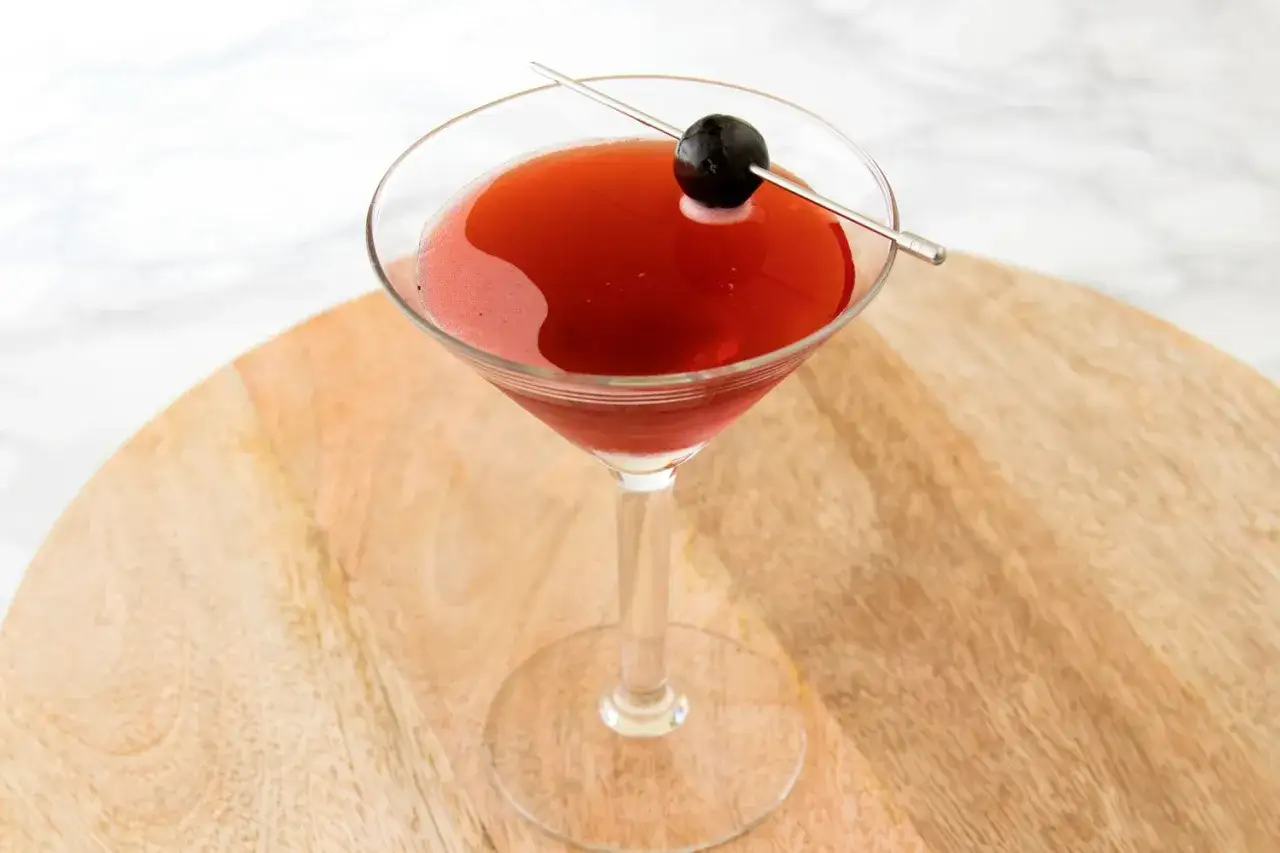Czerwony drink w kieliszku koktajlowym, ozdobiony czarną oliwką na wykałaczce. Idealny drink San Francisco na letnie wieczory.