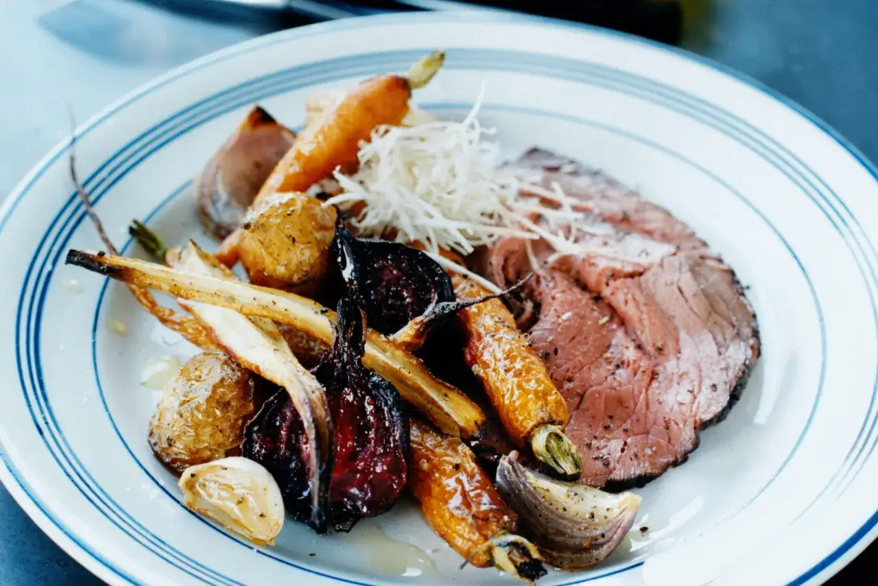 En tallrik med skivad rostbiff, rostade rotfrukter som mor&ouml;tter och palsternacka, samt vitl&ouml;k. Ett perfekt rostbiff recept f&ouml;r en h&auml;rlig middag.
