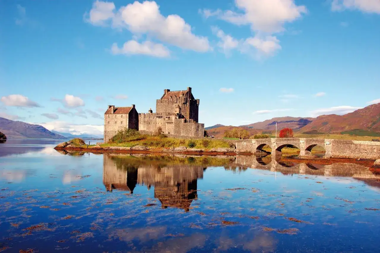 Eilean Donan Castle, perła Szkocji, co zobaczyć na wyspie. Zamek odbija się w spokojnej wodzie, a kamienny most prowadzi do niego.