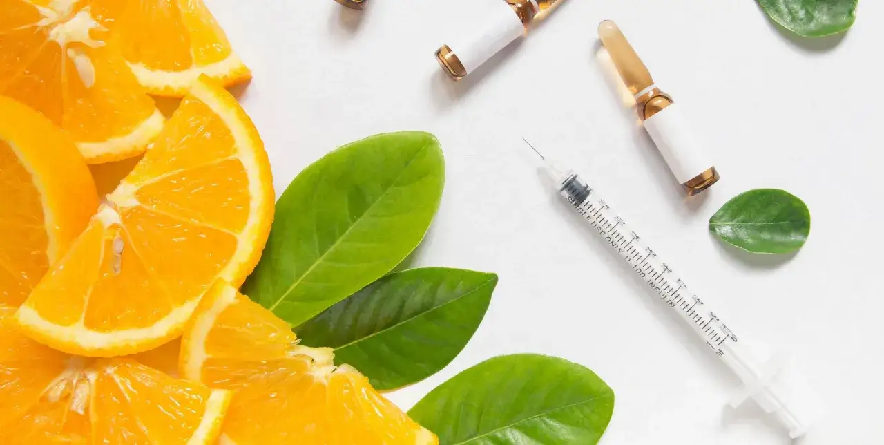 Orangenscheiben, Ampullen und Spritze. Eine Vitamin C-Infusion zahlt Krankenkasse, wenn medizinisch notwendig.