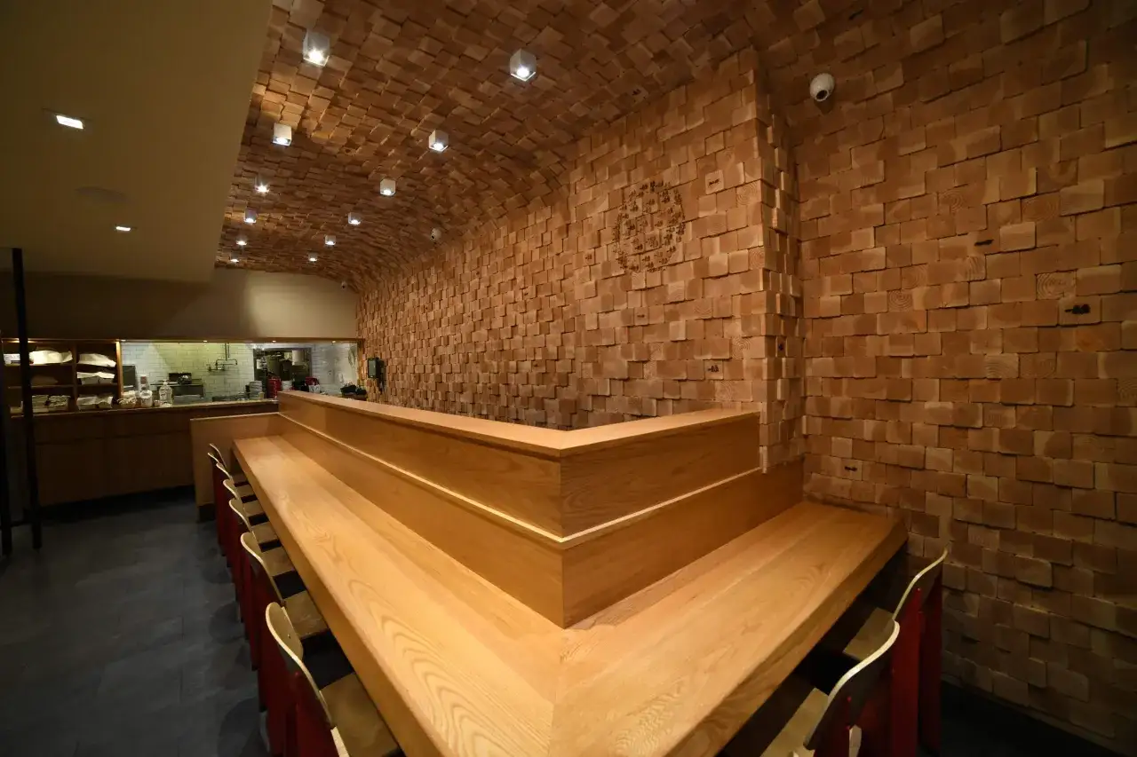 Interno di un ristorante con pareti e soffitto in legno grezzo. Bancone in legno chiaro con sedie rosse. Forse qui si mangia il best ramen in nyc.
