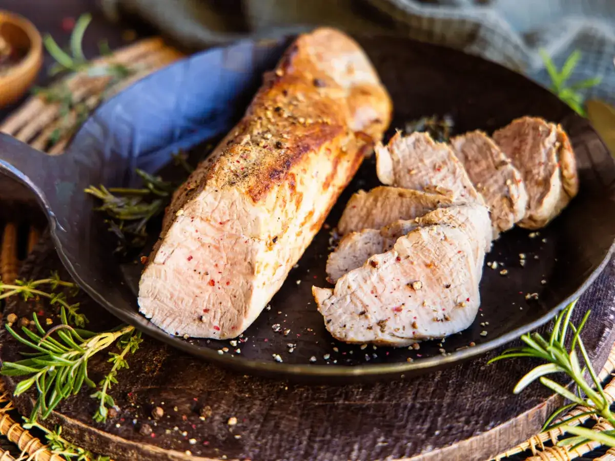 Saftiges Schweinefilet, teilweise aufgeschnitten, in einer Pfanne mit Rosmarin und Pfefferkörnern. Perfekt für Ihre nächsten Schweinefilet Rezepte.