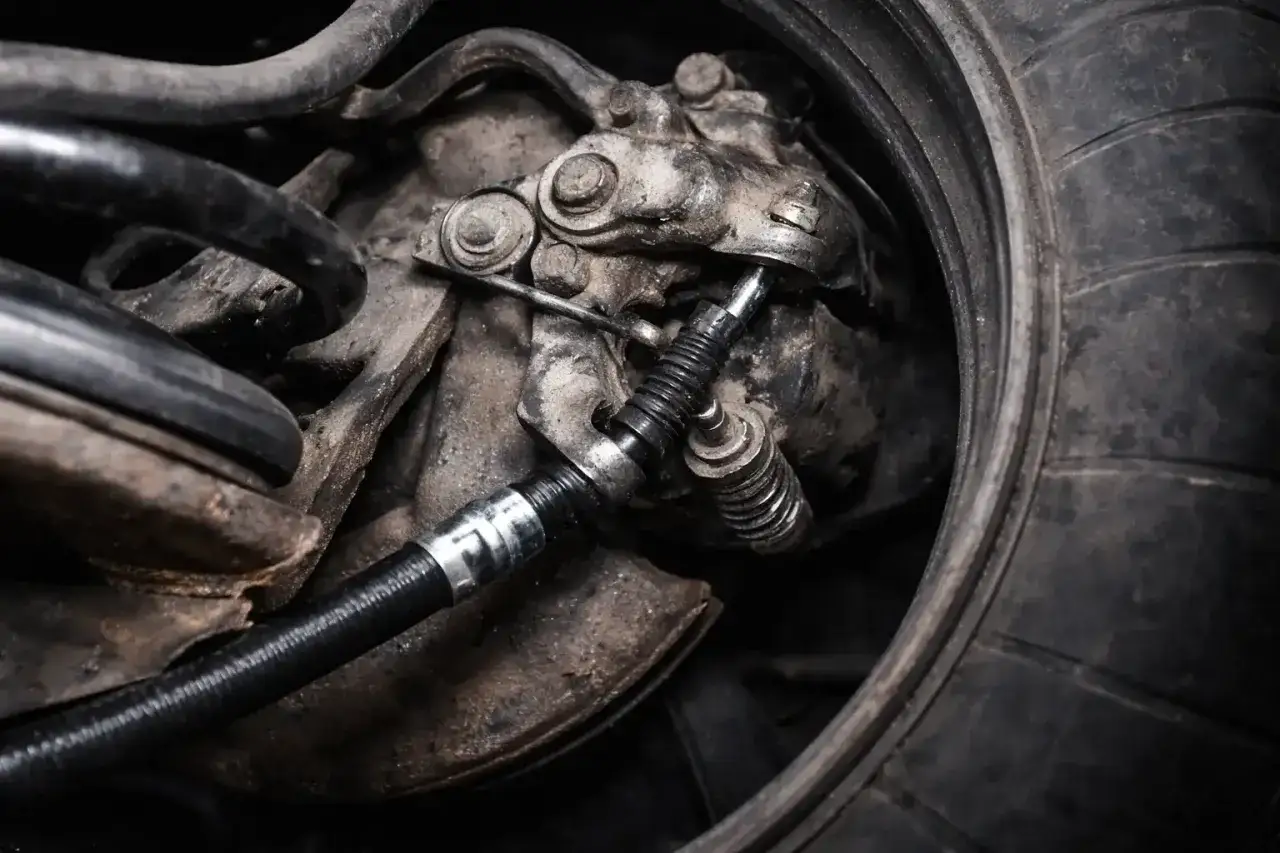 Widok na mechanizm hamulcowy z widoczną wymianą linki hamulca ręcznego.