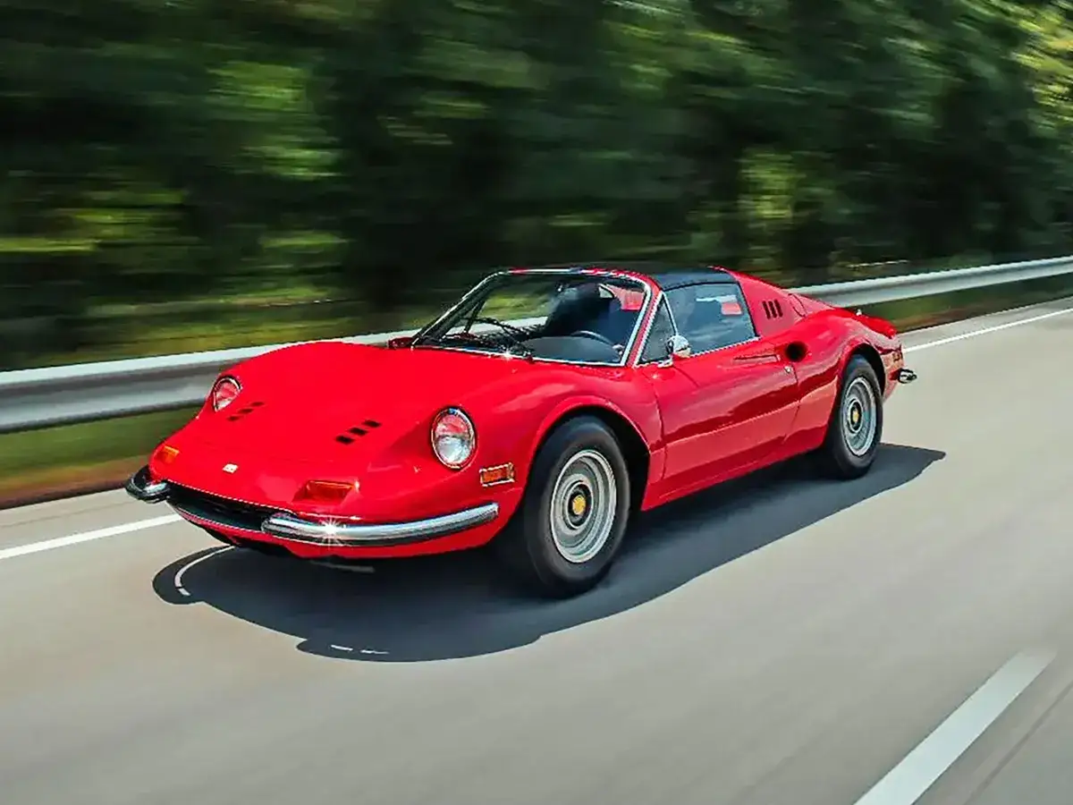 Czerwone Ferrari Dino sunie po drodze, otoczone zielenią.