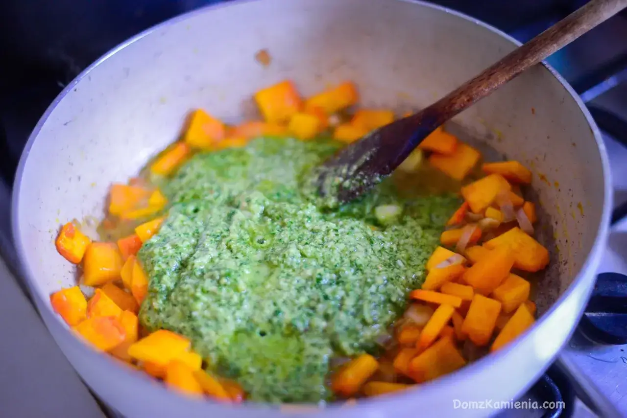 Na patelni gotuje się dynia z zielonym, aromatycznym pesto z rukoli. Drewniana łyżka miesza składniki.