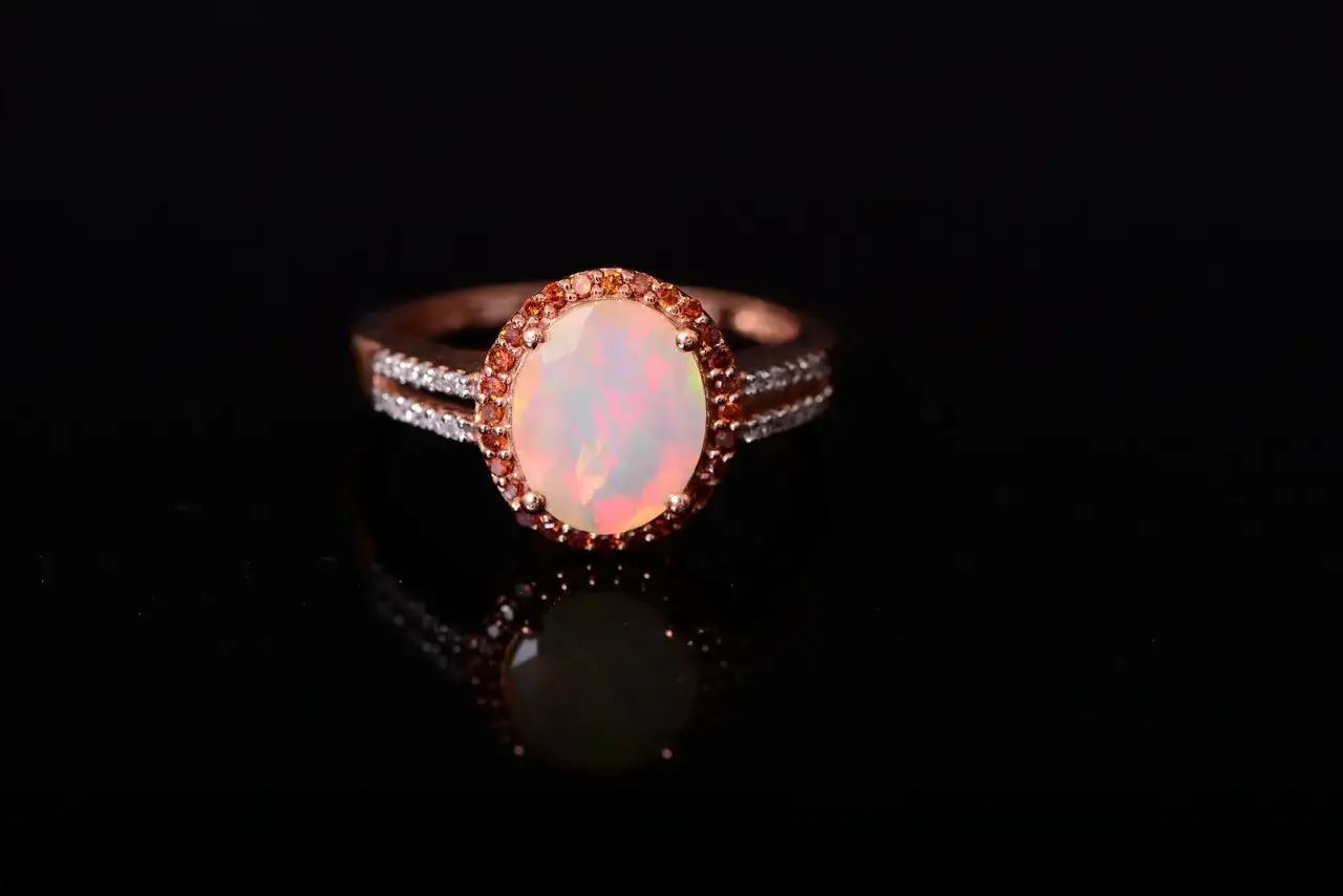 Oval opal ring with a halo of small orange and white stones, perfect for an October 5th birthstone.