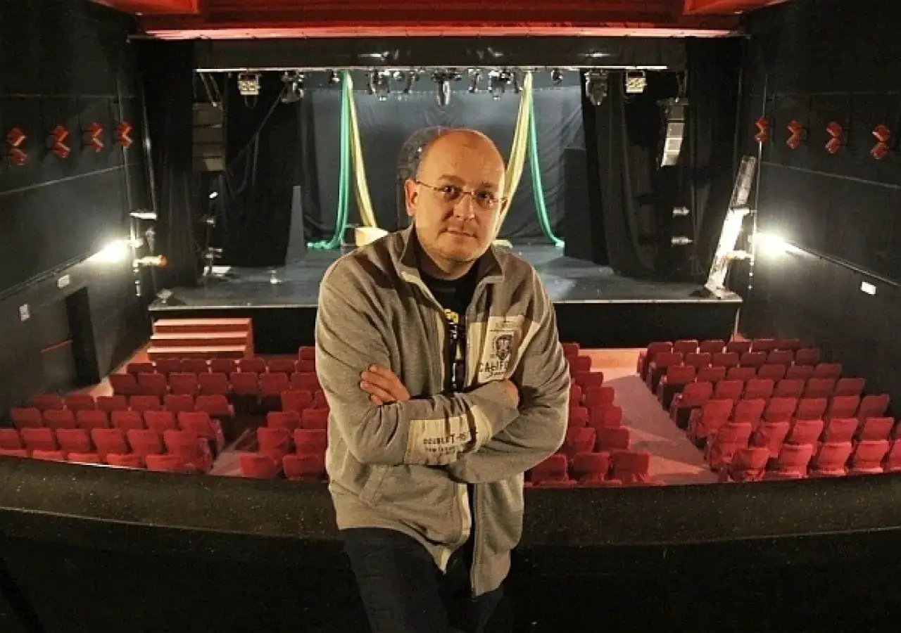 Mężczyzna stoi przed pustą widownią teatru. Widok na scenę i rzędy czerwonych foteli. Teatr Palladium, plan widowni.