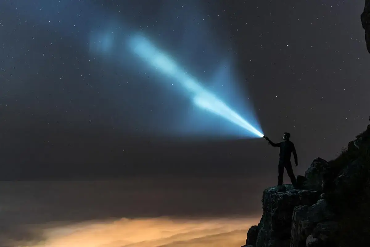 Mężczyzna na skale wysyła sygnał SOS latarką w nocne, gwiaździste niebo.