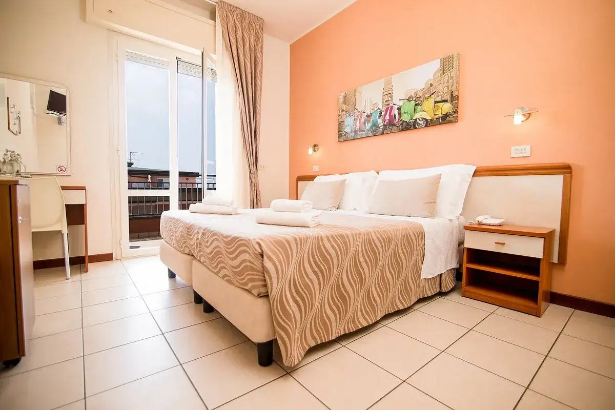 Camera accogliente in un b&b Riviera Romagnola, con letto matrimoniale, quadro di vespe colorate e balcone.