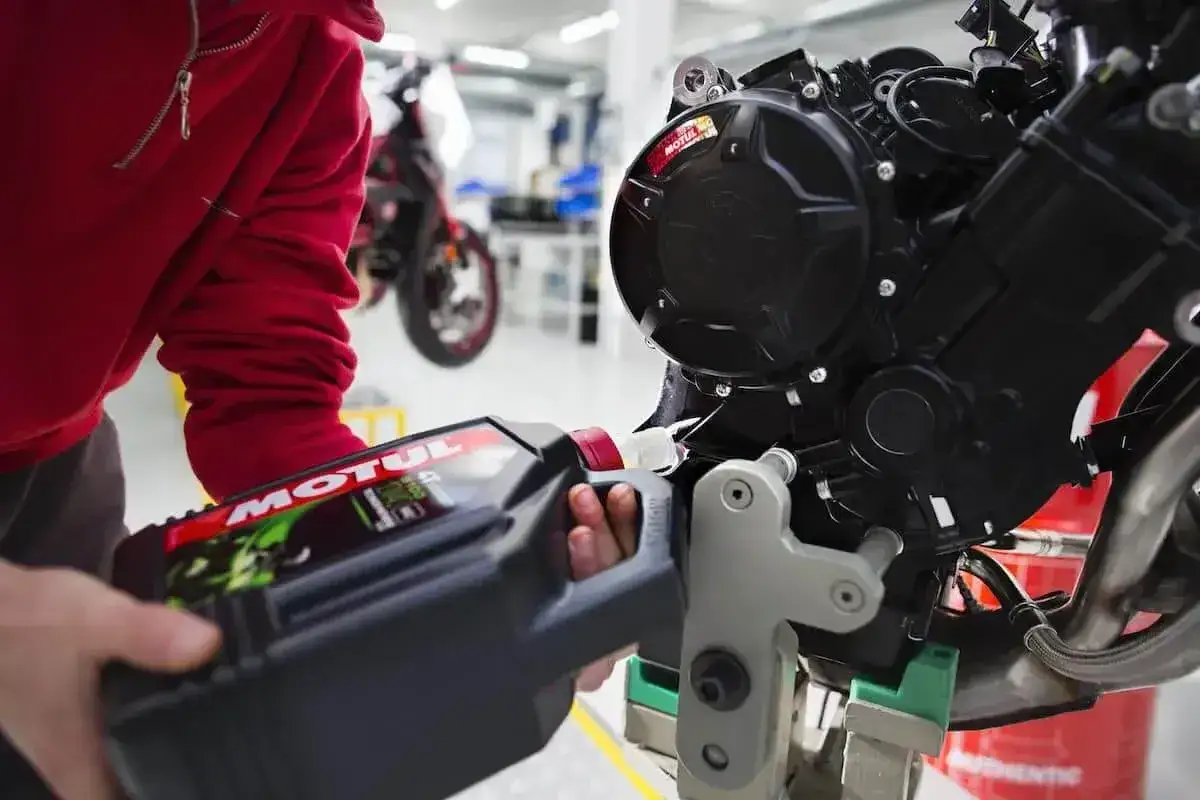 Osoba w czerwonej bluzie nalewa olej Motul do silnika motocykla. Pamiętaj o regularnej wymianie oleju, co ile motogodzin zależy od modelu.