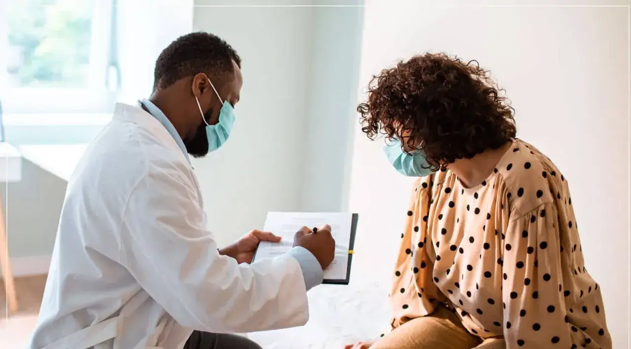 M&eacute;dico con mascarilla explica el tratamiento para la gonorrea a una paciente.