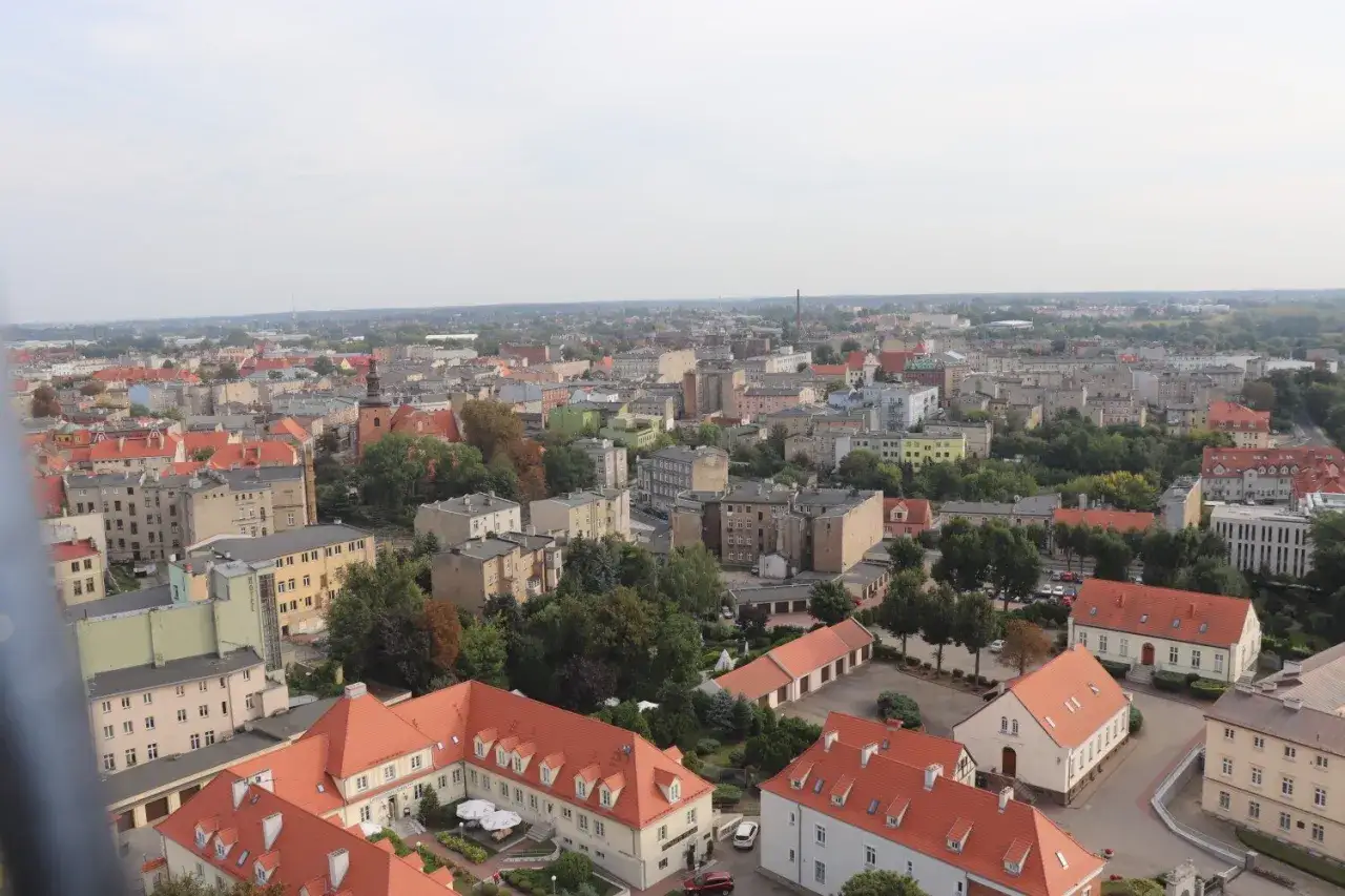 Widok z góry na miasto z czerwonymi dachami, gdzie jest Gniezno. Widać wiele budynków, drzew i ulic.