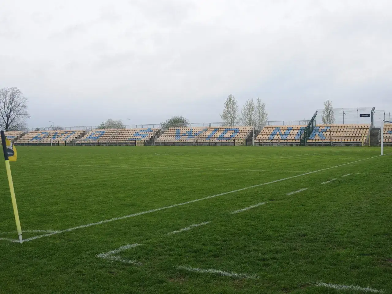 Pusta trybuna stadionu Avia Świdnik czeka na kibic&oacute;w. Zielona murawa i słupki narożne gotowe na mecz.