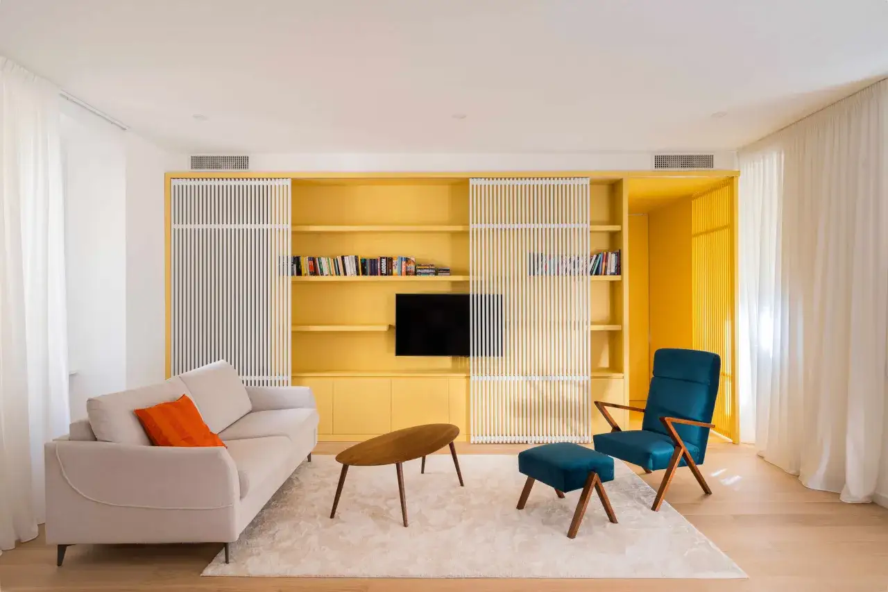 Soggiorno moderno con libreria gialla, divano beige, poltrona blu e tavolino in legno. Un'ispirazione per il colore da abbinare al giallo pareti.