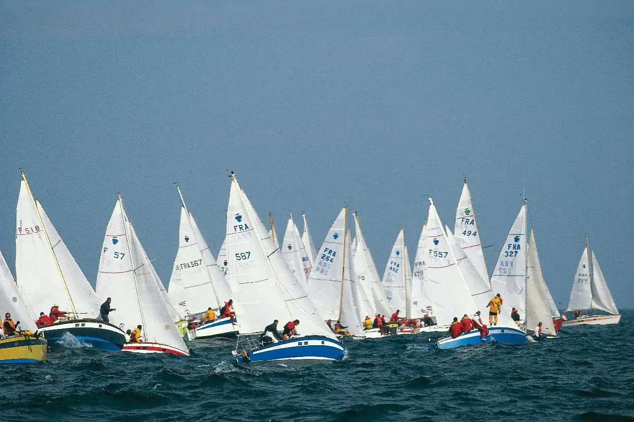 Course de voiliers Muscadet. Une flotte de bateaux blancs navigue sur une mer agitée, sous un ciel bleu clair.