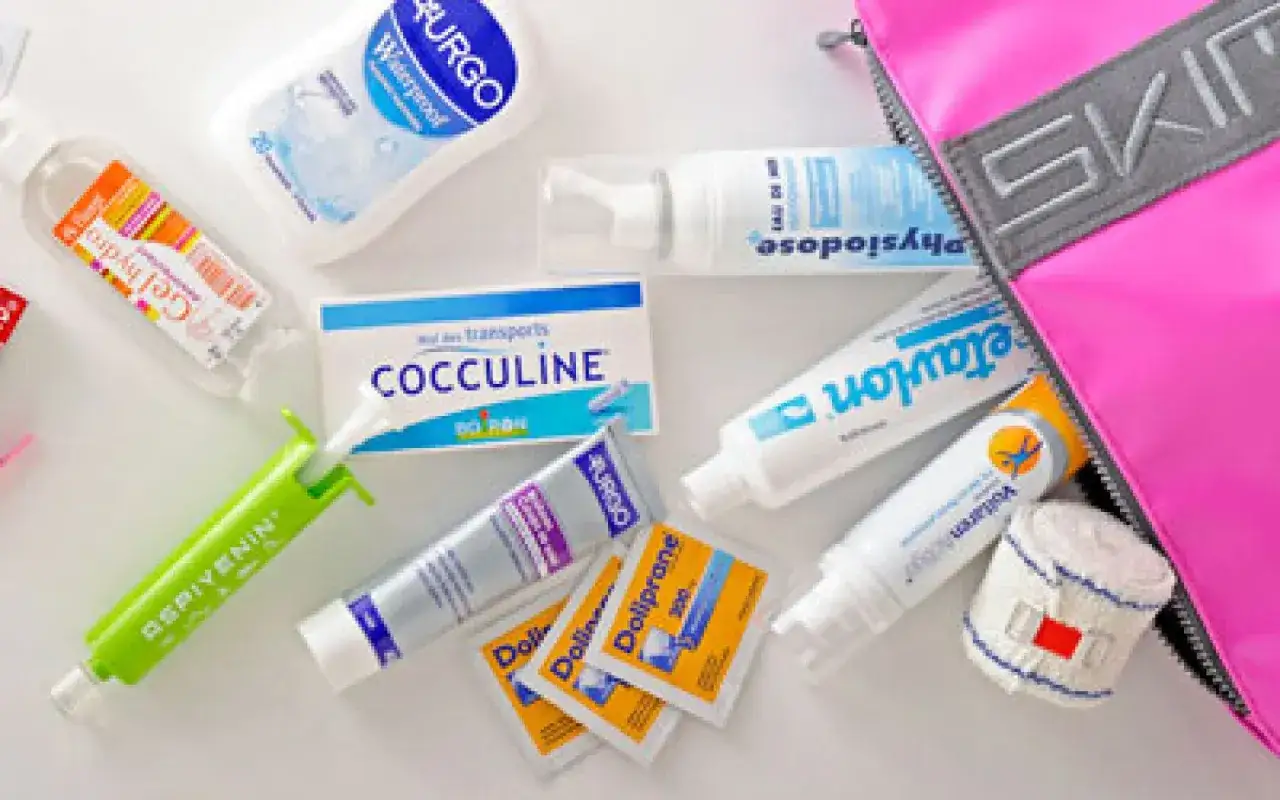 Une trousse de premiers secours avec divers produits : spray, tubes, pansements, et un assistant sanitaire pour les petits bobos.
