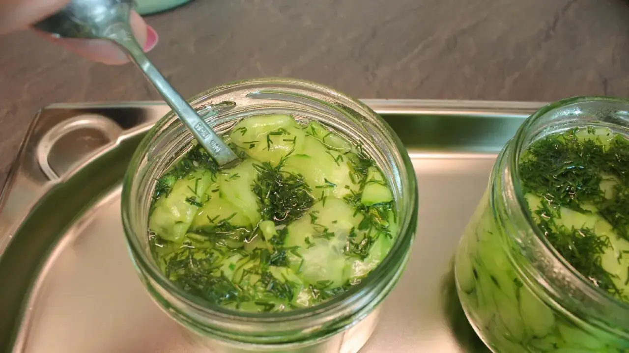 Ein Glas Gurkensalat mit Dill wird mit einem Löffel vorbereitet, um ihn einzukochen.