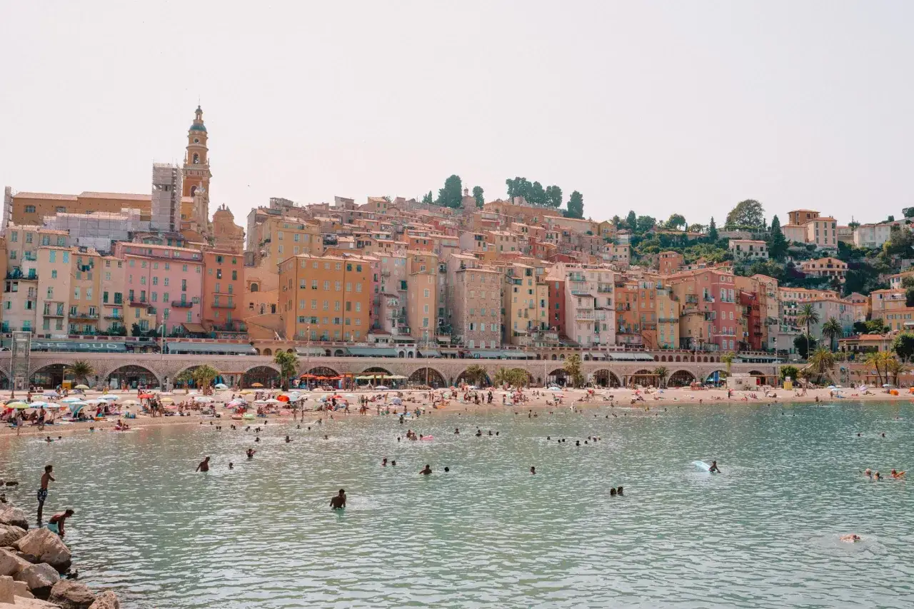 Bunte Häuserfront am Meer, Menschen genießen ihren Frankreich Urlaub am Meer. Ein lebhafter Strand mit Sonnenschirmen und badenden Menschen.