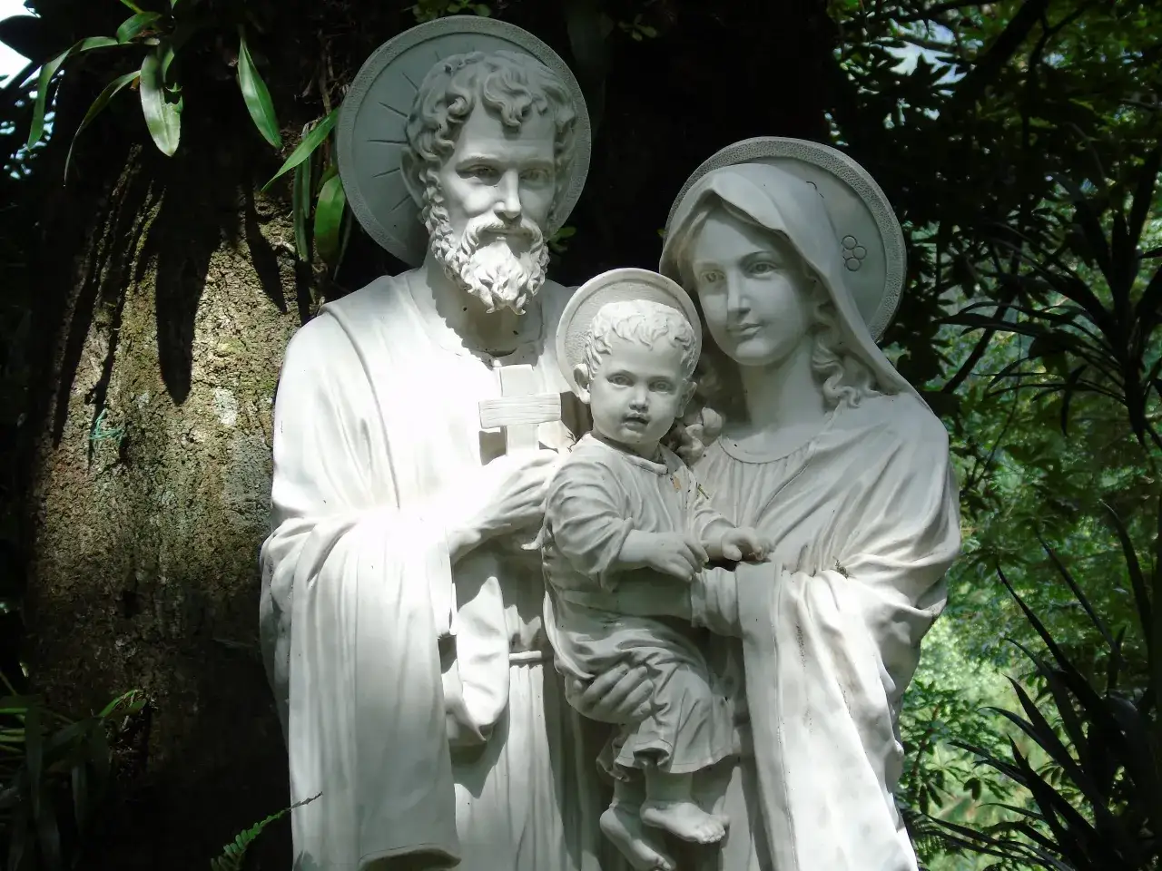 Kamienna Święta Rodzina w otoczeniu zieleni. Rzeźba symbolizuje różnicę między wiarą żywą a tradycją przekazywaną w rodzinie.