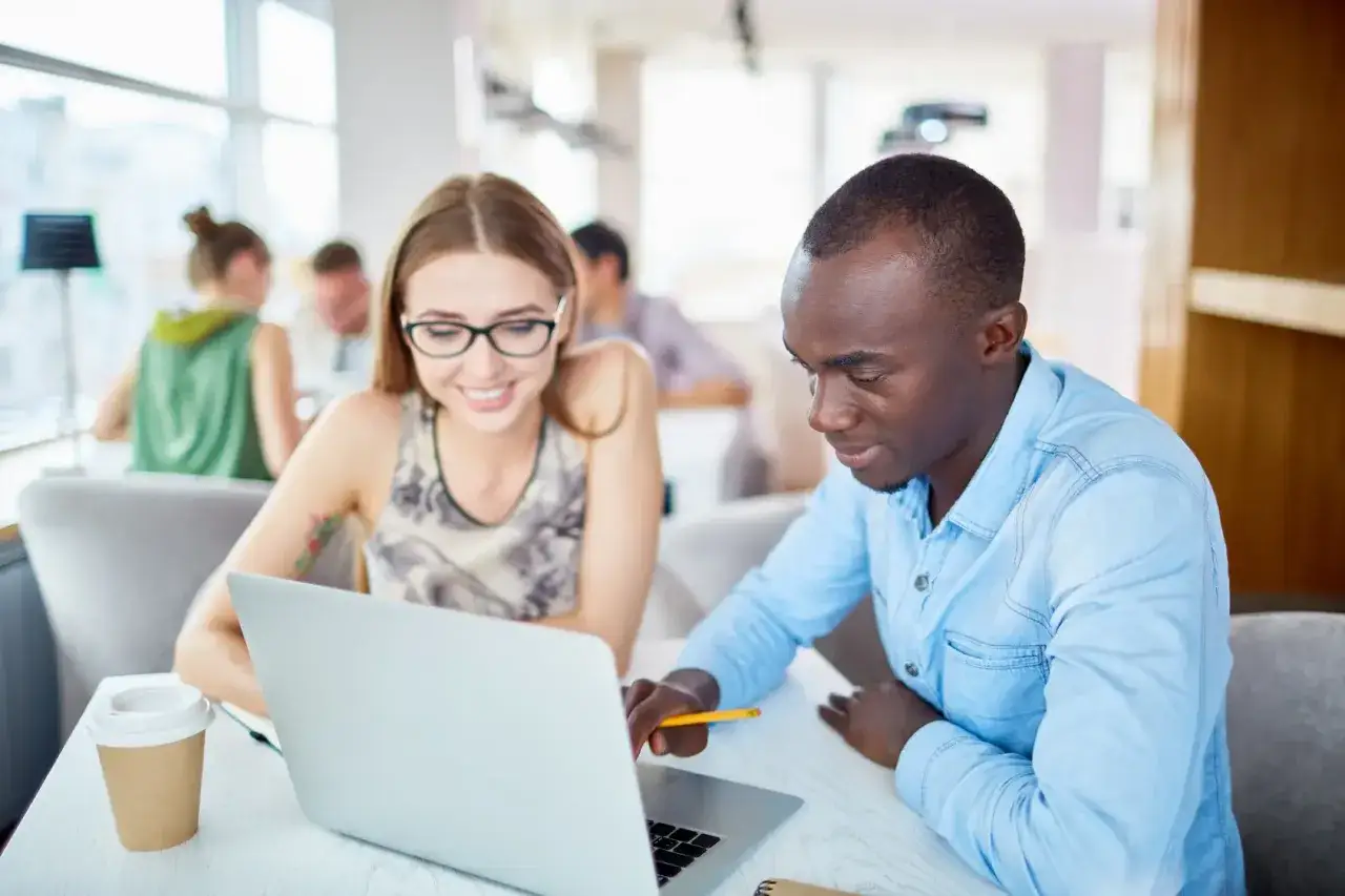 Zwei Studierende arbeiten an einem Laptop, vielleicht f&uuml;r ihr **online Studium Bayern**. Sie sitzen in einem hellen Raum, eine Kaffeetasse steht bereit.