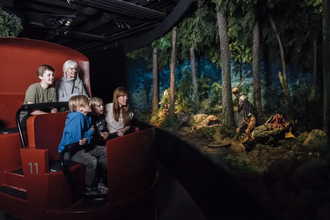 Familj på en åktur i en vikingamuseum i Stockholm, som visar en dramatisk scen med vikingar i en skog.