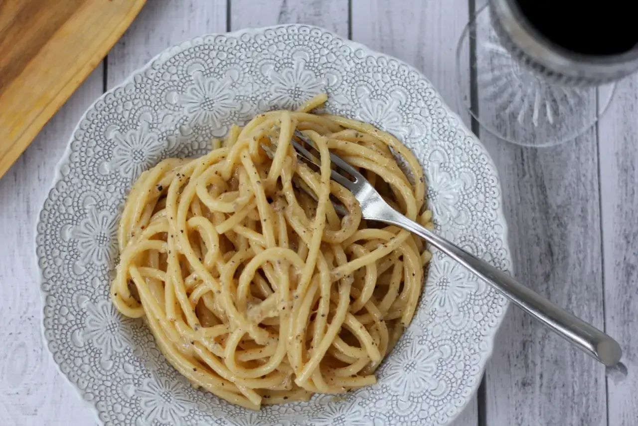 Pyszne cacio e pepe na talerzu z ozdobnym wzorem. Widok z góry na makaron z serem i pieprzem, obok widelec.