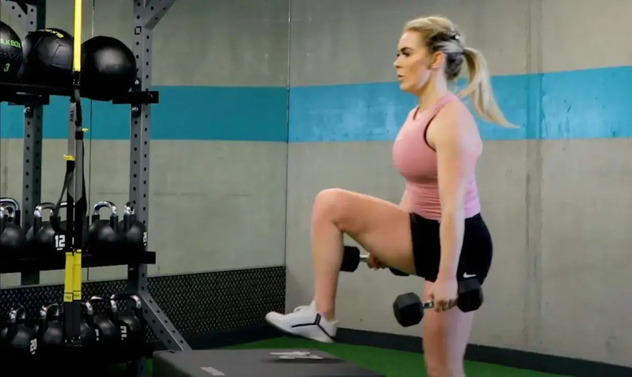 Kvinna utför step ups med hantlar i ett gym.