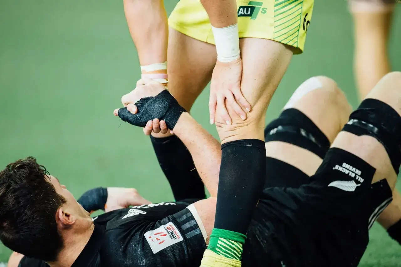 Fizjoterapia w sporcie: zawodnik All Blacks z kontuzją nogi, wspierany przez kolegę z drużyny.
