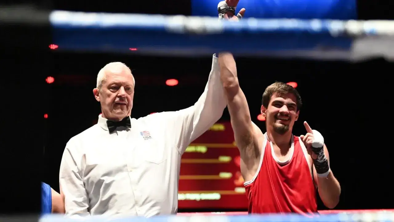 Referee raises the winner's arm in a boxing match. The boxer, smiling, points to the sky, celebrating a victory with no knockdowns.