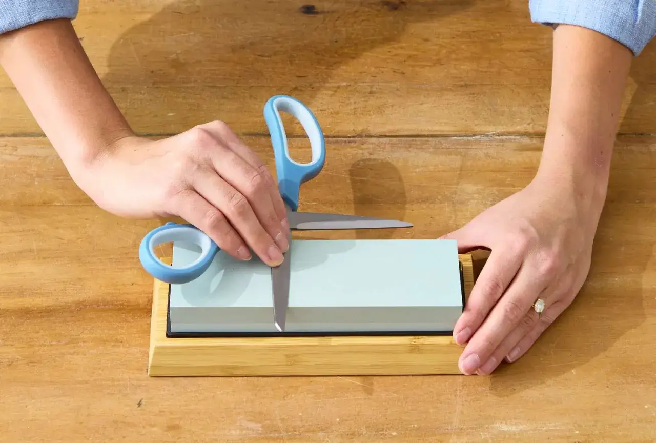 Manos afilando tijeras con piedra de afilar. Aprende c&oacute;mo afilar tijeras con piedra para un corte perfecto.