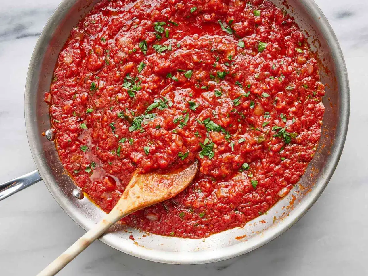 Eine Pfanne mit köstlicher, hausgemachter marinara sauce, garniert mit frischer Petersilie. Ein Holzlöffel rührt die Sauce um.