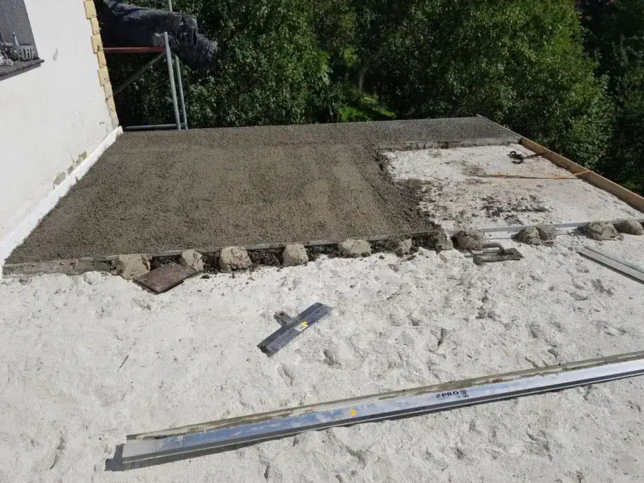 Budowa dachu z styrobetonu: świeża warstwa materiału na konstrukcji, narzędzia budowlane w pobliżu.