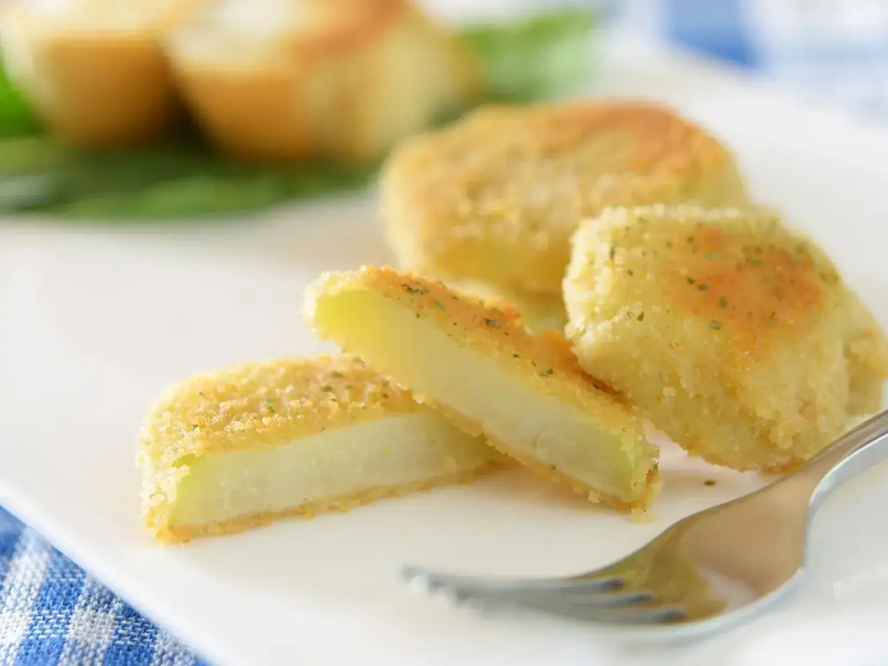 Kohlrabi mal anders: knusprig panierte Kohlrabischeiben, goldbraun gebacken, mit Kr&auml;utern bestreut, auf einem Teller mit einer Gabel.