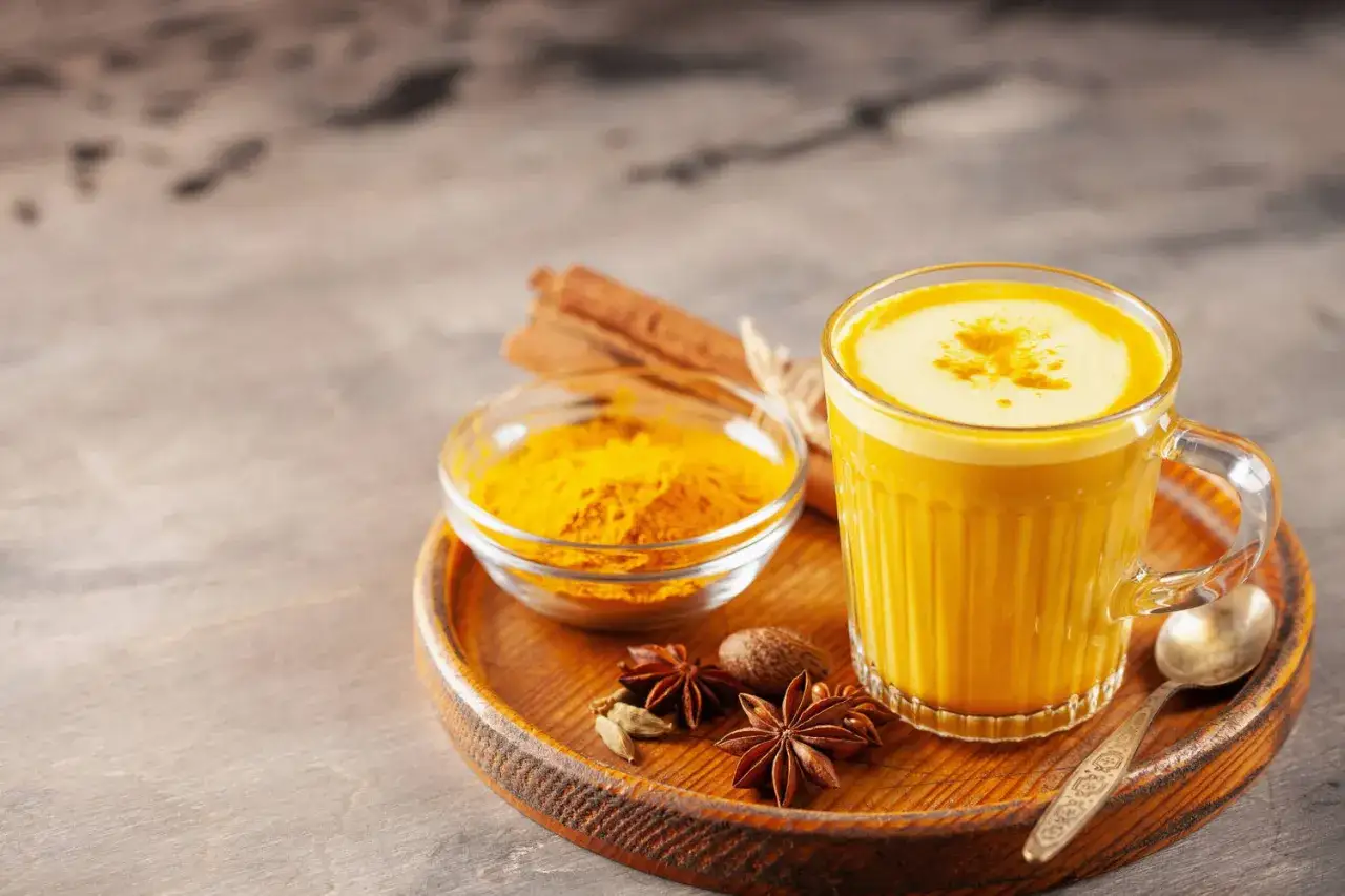 Eine Tasse goldene Milch mit Kurkumapulver, Zimtstangen und Sternanis auf einem Holzteller.