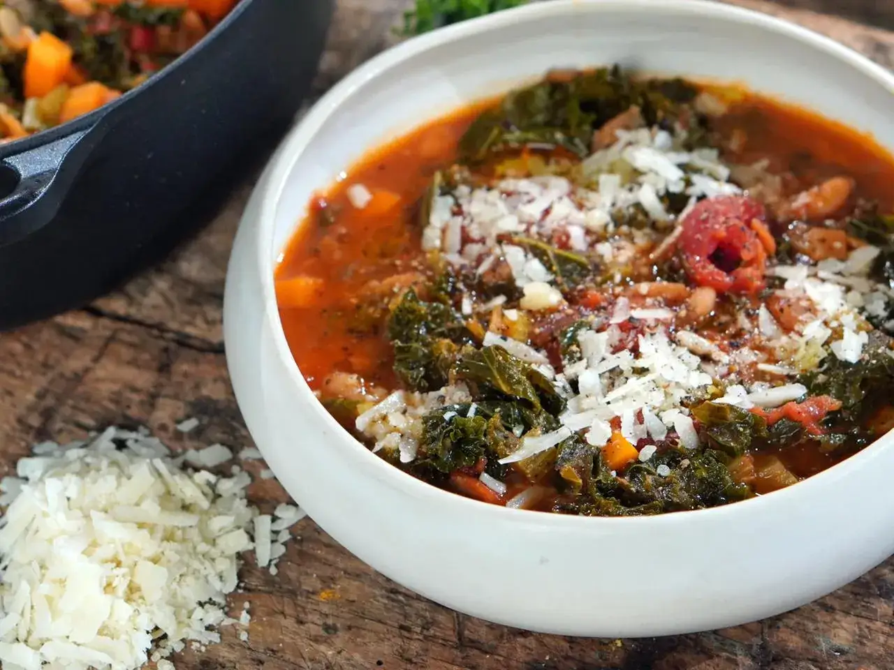 Herzhafte toskanische Bohnensuppe mit Gr&uuml;nkohl und geriebenem Parmesan, serviert in einer wei&szlig;en Sch&uuml;ssel auf rustikalem Holz.